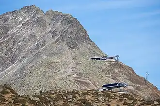 De top van de Bettmerhorn met ten zuiden op de kam een kruis tot waar een wandelpad loopt, het bergstation van de gondelbaan en op de voorgrond een skilift.