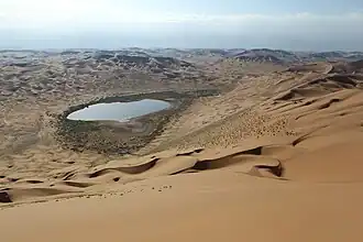 Woestijnlandschap met meer van de Badain Jaranwoestijn met het hoogste punt van de woestijn, de Bilutu Peak op de achtergrond.