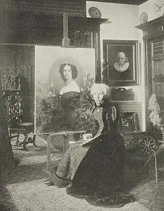 Mevr. Kate Bisschop-Swift in haar atelier bij het door haar geschilderde portret van koningin Sophie (1902)