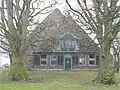 Stolphoeve met breed, uitgebouwd voorhuis en houten schuurwanden. Zeer fraaie erfbeplanting