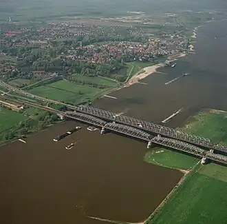 1987: Luchtfoto van de spoorbrug, met daarachter de Bommelse Brug. Ook Zaltbommel is te zien, met de Grote of Sint-Maartenskerk.