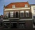 Gepleisterde lijstgevel voor pand van parterre en twee verdiepingen met zadeldak. De bebouwing aan de Markt is van belang voor de situatie van Stadhuis en Hoofdwacht