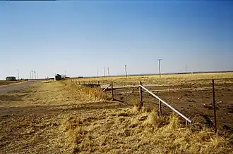 Een uitzicht over een veld in West-Oklahoma, met een aantal gebroken funderingen en graanopslagbakken.