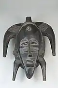Kpeliyee masker van het Poro genootschap. De kop vertoont littekens die als versiering op een gezicht van een vrouw worden aangebracht. De mond steekt naar voren en de tanden zijn zichtbaar.