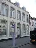 Huis met brede lijstgevel, waarin een ingang en vensters met spiegelbogen in Naamse steen.