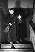 Een vrouw gebruikt een petroleumlamp in een trappenhuis wegens lampenschaarste. Duitsland, 1949.