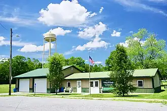 Een foto van een breed vrijstaand gebouw van één verdieping met een watertoren in de achtergrond en een wapperende Amerikaanse vlag.