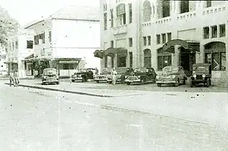 Geparkeerde auto's en militairen bij de Marine Cantine en het kantoor van de NILLMIJ Batavia.