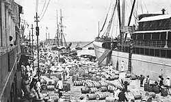 De Amerikaanse S.S. Zulia aangemeerd aan de Handelskade die vol ligt met zakken en vaten (tussen 1900 en 1910)