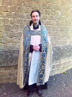 Priester in de 21ste eeuw in lofkledij: albe, amict, cingel, stola en koorkap.