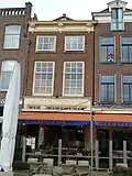 Winkelwoonhuis met voorgevel uit 19de eeuw in een sobere eclectisch-classicistische bouwtrant. Achterste gedeelte met gevel aan de Voldersgracht in opzet ouder, mogelijk uit de 17de eeuw of eerder.