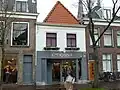 Winkelwoonhuis, in oorsprong mogelijk 17de-eeuws of ouder, met voorgevel in 19de-eeuwse traditioneel-classicistische vormen. Winkelpui uit 1986. Het pand is voor de gemeente Delft van algemeen belang vanwege de herkenbaarheid van de lokaaltopografische ontwikkeling.