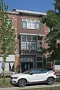 Bedrijfspand met bovenwoning, in 1929 ontworpen en gebouwd door bouwkundige en aannemer C. Vlasbom, in een strakke bouwstijl met invloeden van de Haagse School.