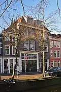 Bedrijfspand met bovenwoningen, rond 1920 gebouwd in een traditionalistische bouwtrant, hoofdstructuur mogelijk ouder.