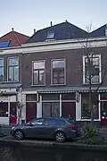Winkelwoonhuis, gebouwd in een sobere traditioneel-classicistische trant vermoedelijk in 1887 als uitbreiding van het rechts belendende pand. Het pand is met het rechts belendende pand voor de gemeente Delft van algemeen belang vanwege de cultuurhistorische waarde. Het is van belang als goed en gaaf voorbeeld van een winkelwoonhuis in traditionalistisch-classicistische vormen uit de tweede helft van de 19e eeuw. Het pand is met het rechts belendende pand van belang als ensemble van een dubbel bedrijfspand met bovenwoning dat in 1887 het huidige uiterlijk kreeg.