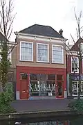 Winkelwonhuis, in oorsprong 17de-eeuws of ouder. Voorste gedeelte gemoderniseerd in de 18de eeuw en voorzien van een lijstgevel in Lodewijk XIV- vormen. Pui in 1920 ontworpen door E.H. Luxemburg.