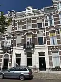 Pand in neorenaissance trant met in de gevel banden, getoogde en geprofileerde vensterbekroningen en een balcon op consoles met ijzeren hekje. Boven de kroonlijst een dakkapel met rolwerk. Gepleisterde parterre