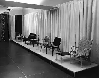 Zwart-wit foto van meubeltentoonstelling. Op de foto staan meerdere stoelen en een salontafel naast elkaar gepresenteerd.