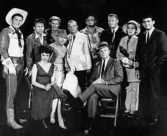 cast van de Dick Powell show, najaar 1961, van de aflevering Who Killed Julie Greer?. van links naar rechts: Ronald Reagan, Nick Adams, Lloyd Bridges, Mickey Rooney, Edgar Bergen, Jack Carson, Ralph Bellamy, Kay Thompson, Dean Jones. Zittend van links: Carolyn Jones en Dick Powell.