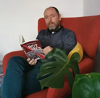 Auteur Dieter Rogiers leest een exemplaar van Bot mes in een rode oorfauteuil.