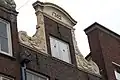 Pand met halsgevel met gebeeldhouwde vleugelstukken en gebogen fronton en met jongere onderpui