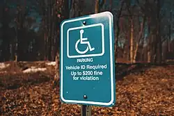 Pictogram met het internationaal erkende symbool voor toegankelijkheid (witte rolstoel op blauw vlak). Duidt een gereserveerde parkeerplaats aan voor personen met een handicap. Inclusief boetebepaling.