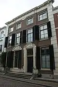 Pand met brede lijstgevel van vier vensterassen, parterre met twee verdiepingen, middenrisaliet en hoekpilasters