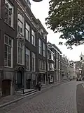 Pand met eenvoudige lijstgevel met zijpilasters, rijk geprofileerde kroonlijst en in de mezzanino vensters, die in de kroonlijst doorlopen