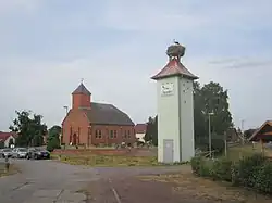 Dorpsbeeld met ooievaar op trafohuisje te Grütz. Het kerkje dateert van 1806.