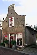 Pand met ingezwenkte gevel, bekroond door een geprofileerde topdekplaat. Vensters met rode strekken in het Ysselstenen metselwerk. Aan de achterzijde een puntgevel met vlechtingen