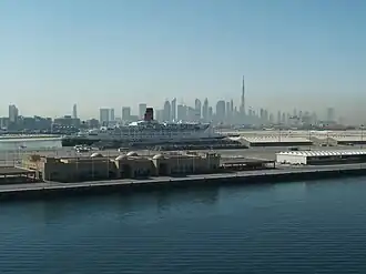 De Queen Elizabeth 2 in Port Rashid met op de achtergrond de skyline van Dubai