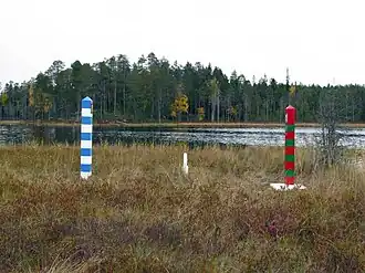 Grenspalen op het eiland: de blauw-witte paal van Finland en de rood-groene paal van Rusland