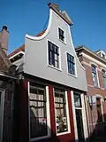 Bakstenen huis voorzien van een houten klokgevel, met gebroken fronton. Ingang met bovenlicht in een omlijsting met geblokte pilasters