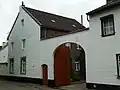 Hoeve van baksteen om gesloten binnenplaats. Aan de straat een puntgevel en een muur met poortje en inrijpoort. Segmentboogvenster in Naamse steen