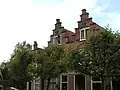 Huis met trapgevel, toppilaster op een maskerkraagsteen.Tweelichtzoldervensters, met een luik van geprofileerde planken. Trapgevel gekoppeld met die van buurnummer 7