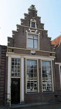 Pand met bakstenen trapgevel met in het fries drie gevelstenen