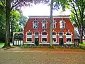 Woonhuis gebouwd als café bij het Zuidkamp van vliegveld Twente. Het woonhuis is opgetrokken vanuit een rechthoekige plattegrond in baksteen op plint, over één bouwlaag