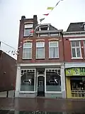 WINKEL/WONING, gelegen aan De Heurne, gebouwd in 1912 in art-nouveaustijl. In 1929 werd de winkelpui gewijzigd waarbij de entree naar de linkerzijde verplaatst. In 1981 is het pand gerestaureerd en werd de entree weer naar de originele plaats gezet.