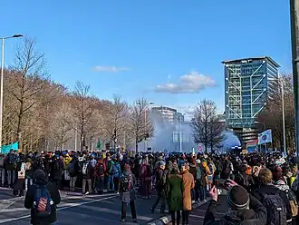 Foto van protest. Veel mensen op een snelweg, in de achtergrond is een waterkanon die op de benevelstand spuit zichtbaar.