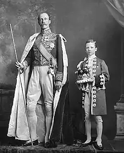 De graaf van Chesterfield in ceremoniële hofkleding en kroningsgewaad. Als Lord Steward of the Household (een hoge functie aan het hof) heeft hij het recht een witte staf te dragen. Zijn page Ferdinand Fairfax draagt zijn adelskroon (1911)[30]