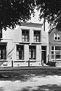 Huis met gepleisterde lijstgevel met ingezwenkte top. Schuifvensters. Houten stoeppalen, verbonden door ijzeren stangen