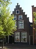 Pand onder zadeldak tegen trapgevel met toppilaster op kopje