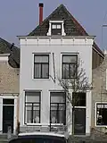 Woonhuis onder schilddak met gepleisterde lijstgevel en voordeuromlijsting met gecanneleerde pilasters