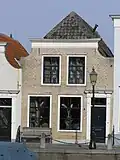 Huis met gepleisterde ingezwenkte lijstgevel. Schuifvensters. Voordeuromlijsting