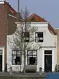 Huis met geverfde ingezwenkte lijstgevel. Staafankers. Voordeuromlijsting