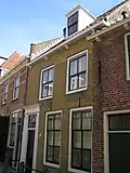 Pand met verdieping en zadeldak. Sobere lijstgevel, waarin deuromlijsting met verdiepte pilasters en hoofdgestel