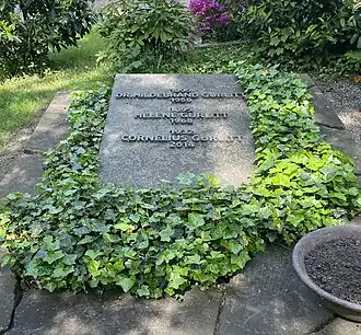 Foto van de grafzerk van Hildebrand Gurlitt. De grijze steen ligt op de grond en toont de namen, geboorte- en sterfjaren van Hildebrand Gurlitt, Helene Gurlitt en Cornelius Gurlitt. Rondom het graf groeit klimop.