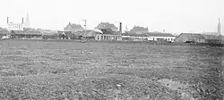 Het emplacement van station Groningen gezien vanuit het westen in 1908. Links de schoorstenen van de koffie- en theefabriek van Niemeyer. Middenachter het stationsgebouw en rechtsachter de Sint-Jozefkathedraal. Daarvoor de spoorgebouwen op het emplacement, waaronder de vetgasfabriek met schoorsteen. Op de voorgrond de weilanden waar in de jaren 1960 het Emmaviaduct werd gebouwd.