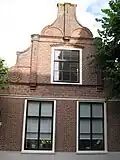 Huis. In- en uitgezwenkte topgevel met gemetselde pilasters en voluten. Pui gewijzigd