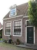 L-vormig huis, in hoofdzaak. Twee ingangen met vroeg-19e-eeuwse deur en snijraam. Drie dakkapellen met gebogen doorbroken frontons. Inwendig vier gesneden laatgotische sleutelstukken